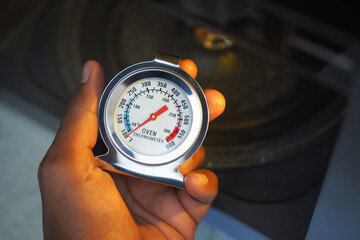 Close-Up of Hand Holding Oven Thermometer in Kitchen