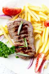 Grilled Steak with french fries and fresh tomatoes. White wooden background.