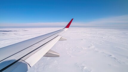 Fototapeta premium Aerial view from airplane wing over snowy landscape and blue sky.