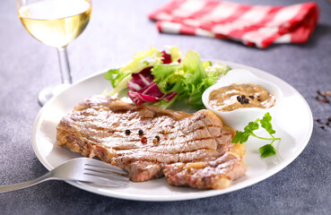 grilled steak, pepper sauce and salad, glass and fork of wine on table