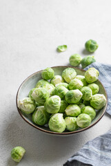 Fresh brussels sprouts in a bowl on a light gray background with napkin. Vegetarian healthy food concept.
