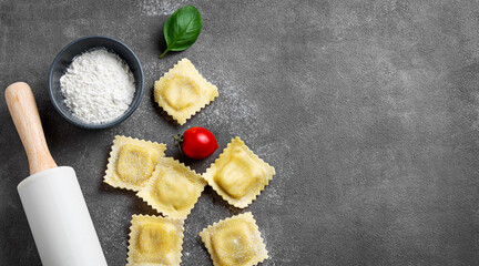 Flat lay of pasta ravioli with tomato and basil on dark background with flour and rolling pin.