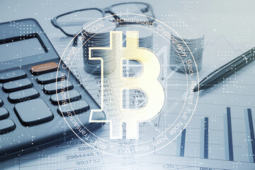 Bitcoin symbol overlaying office desk with calculator, pen, and stacked coins on financial documents, related to cryptocurrency and finance.