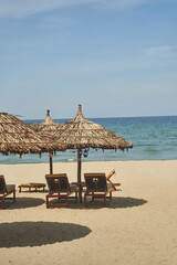 Straw sunshades and sunbeds on the empty pebble beach with sea in the background. Deserted beach with rattan sun loungers and umbrellas