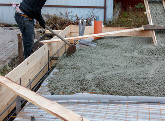 A man is laying concrete on a wooden board