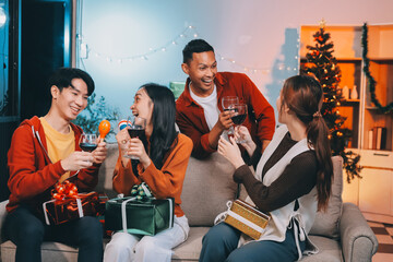 Group of young Asian man and women as friends having fun at a New Year's celebration, holding gift boxes standing by Christmas tree decoration, midnight countdown Party at home with holiday season.