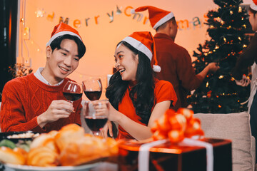 Group of young Asian man and women as friends having fun at a New Year's celebration, holding gift boxes standing by Christmas tree decoration, midnight countdown Party at home with holiday season.