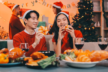 Group of young Asian man and women as friends having fun at a New Year's celebration, holding gift boxes standing by Christmas tree decoration, midnight countdown Party at home with holiday season.