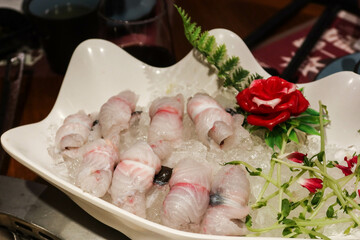 close up of Chinese raw uncooked eel fish in sliced roll with flower and leaf on the side as decoration in a white plate. The ingredient is ready for hot pot.