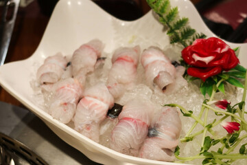 close up of Chinese raw uncooked eel fish in sliced roll with flower and leaf on the side as decoration in a white plate. The ingredient is ready for hot pot.