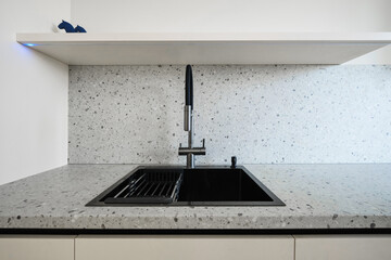 Modern kitchen sink area featuring speckled countertop with black and silver appliances