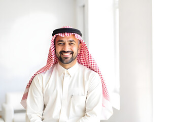 Arabic man in traditional white clothes in his 40s smiling and standing inside of a bright office and looking in the camera