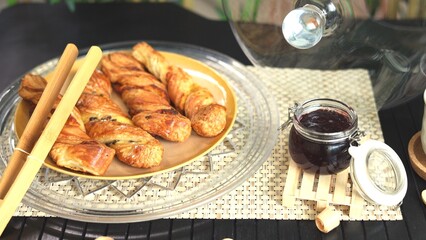 Organic gluten-free breadsticks on crystal plate with wooden bread tongs, accompanied by jar of homemade berry jam, showcasing natural, wholesome ingredients in rustic, refined presentation.