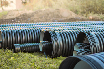 Rows of large black drainage pipes arranged on a grassy construction site. The pipes are ready for...
