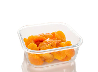 Sweet dried apricots in a glass container, close-up, isolated on a white background.