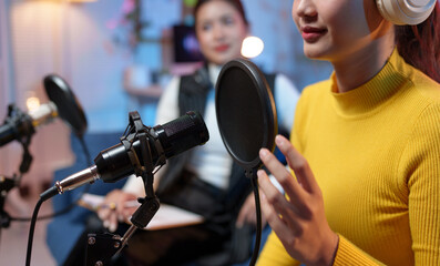 Two Asian women are enjoying recording a podcast together using professional microphones and...
