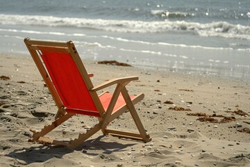 Fototapeta premium Empty red beach chair is sitting on the sand on a sunny beach, waiting for someone to come and relax