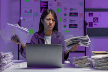 A tired, sleepy, bored businesswoman sits at a desk for a long time, working with a pile of papers. Lots of documents piled up on desks and laptop computers. Office syndrome concept.