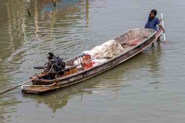 A woman sits on the prow of a boat and is paddling with a paddle, Thailand