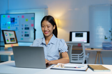 Attractive asian businesswoman sitting working with laptop computer on desk in business growth finance concept Happy marketing plan and customer segments in the office.