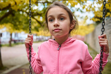 Young girl in pink hoodie on a swing in autumn park