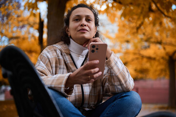 Woman in autumn park using smartphone with thoughtful expression