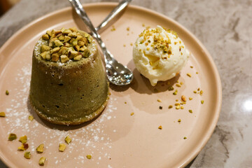 close up of dessert pistachio lava cake with vanilla ice cream on the side and nuts as toppings with two spoons on the plate