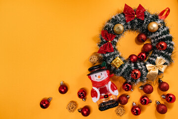 Festive arrangement with a snowman figurine, holiday wreath, and decorations, perfect for Christmas-themed projects on a vibrant orange backdrop.