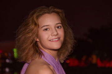 Portrait of a young smiling girl with an open look, illuminated by soft light, on a dark background of a night city