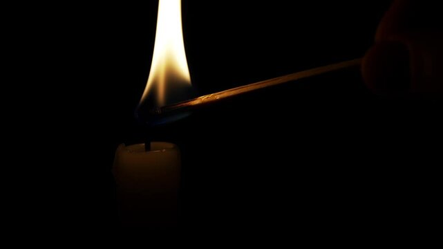 Match ignites a white candle wick, creating a warm glow. The candle stands out against a black background, enhancing its elegance and tranquility in a serene atmosphere