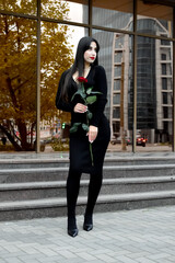 A young woman in a black dress holding a red rose on the street, creating a festive and romantic atmosphere, the perfect look for gifts and special moments.