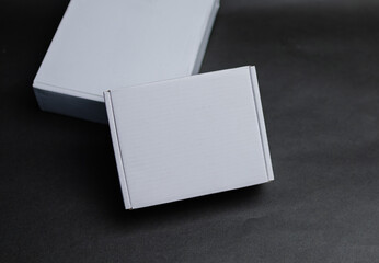 Two white boxes lying flat on a surface The smaller box is on top of the larger box The larger box...