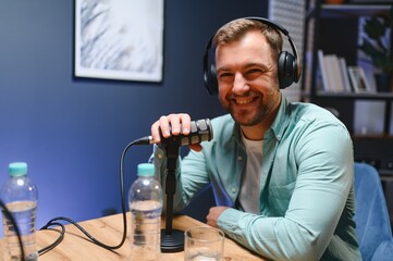 Man podcaster influencer blogger smiling while broadcasting his live audio podcast in studio using...