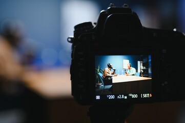 Focus on the camera filming the men's podcast in a professional podcast studio.