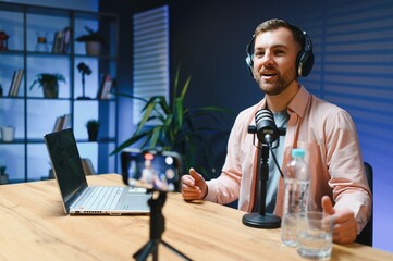 Man podcaster influencer blogger smiling while broadcasting his live audio podcast in studio using...