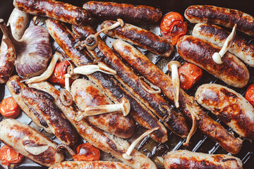 German cuisine. Grill pan with delicious homemade chicken, beef and pork sausages, with mushrooms and tomatoes on the table, close-up