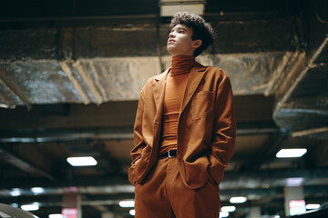 Young man in a stylish brown suit stands confidently under industrial lighting