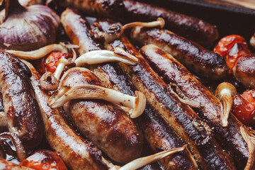 German cuisine. Grill pan with delicious homemade chicken, beef and pork sausages, with mushrooms and tomatoes on the table, close-up