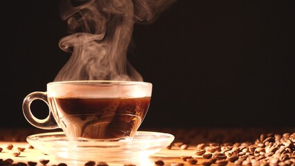 Closeup of a cup of hot coffee with coffee beans, steam rising, set on a saucer, featuring a brown mug and black beverage, isolated on a dark, black background, evoking a cozy aroma of morning warmth