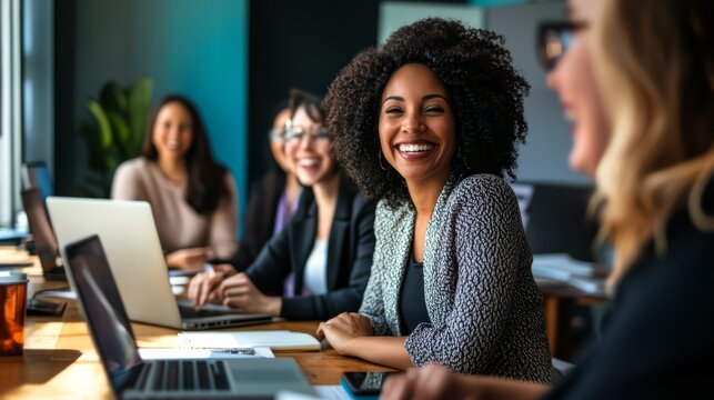 Empowered Women in Tech: A diverse group of smiling women collaborate on laptops in a modern office, showcasing female empowerment and teamwork in the tech industry.