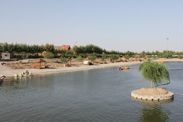 Calm lake with wooden benches by the shore, highlighting peaceful rural landscape and quiet atmosphere under the clear sky.