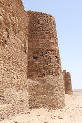 Crumbling stone fortress wall in desert, symbolizing historical resilience and the rugged beauty of ancient architecture.