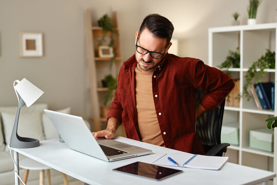 Man working from home suffering backache while using laptop