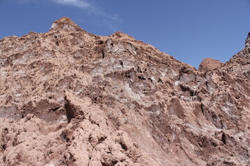 Distant mountains under a blue sky in a desert, with rough terrain and rugged rocks dominating the scene.