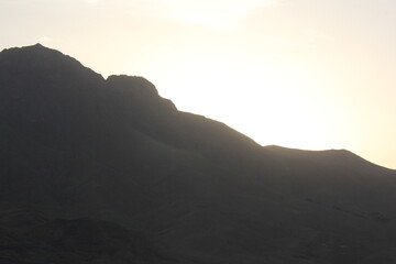 Fototapeta premium Golden sunset behind mountains, casting warm light over the peaks and creating a beautiful, calming natural scene.