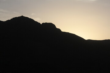 Silhouetted mountain peaks during sunset, creating a dramatic and serene atmosphere, perfect for landscape and wilderness photography collections.