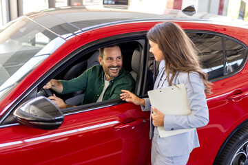 Happy middle age businessman buying new and luxury car. Beautiful female dealer helps him to make...