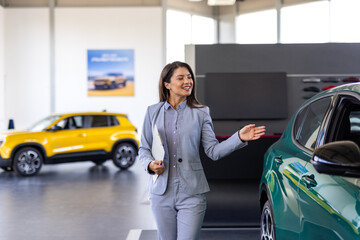 Portrait of a female car saleswoman working in the showroom. Close up of a businesswoman standing next to car in the showroom. Female manager in car dealership