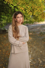 A beautiful fashionable young blonde girl stands in an autumn park on leaves in a gray dress and sneakers