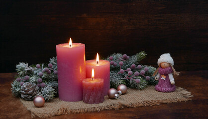 Christmas background: Pink Christmas balls with fir branches and a small doll in front of a rustic wooden wall with space for text.